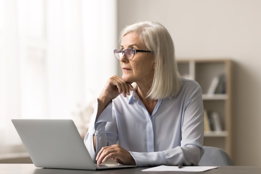 Ältere Dame sitzt beim Laptop und denkt nach