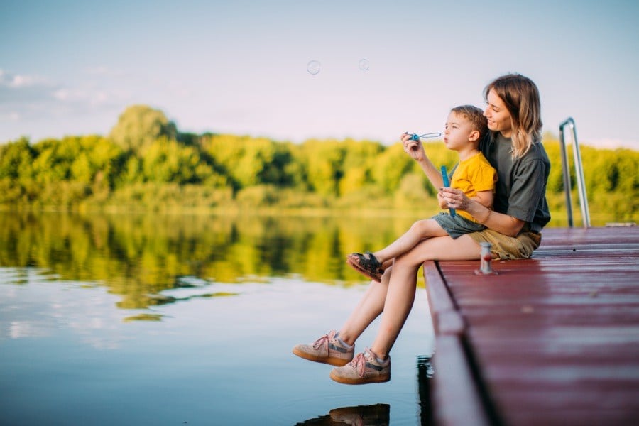 Mutter mit Kind sitzen auf einem Steg bei einem See