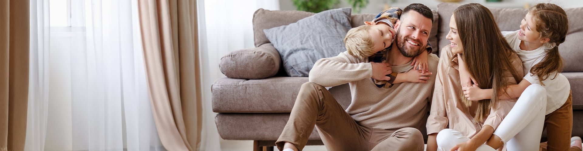 Familie zu viert lacht und sitzt auf der Couch